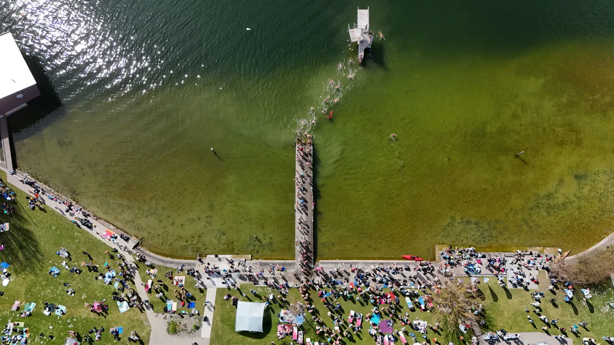Blick von oben auf die Seebadi Niederuster: Zahlreiche Teilnehmende versammeln sich auf der Liegewiese vor dem Sprung ins kalte Wasser. Blaueierschwimmen 2026